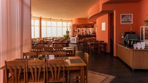 A restaurant with wooden tables and chairs, a bar area, and large windows allowing natural light. - Sun City Hotel (Sunny Beach)