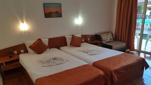 A hotel room with two beds, a sofa, a small table, and a view of the pool. - Sun City Hotel (Sunny Beach)