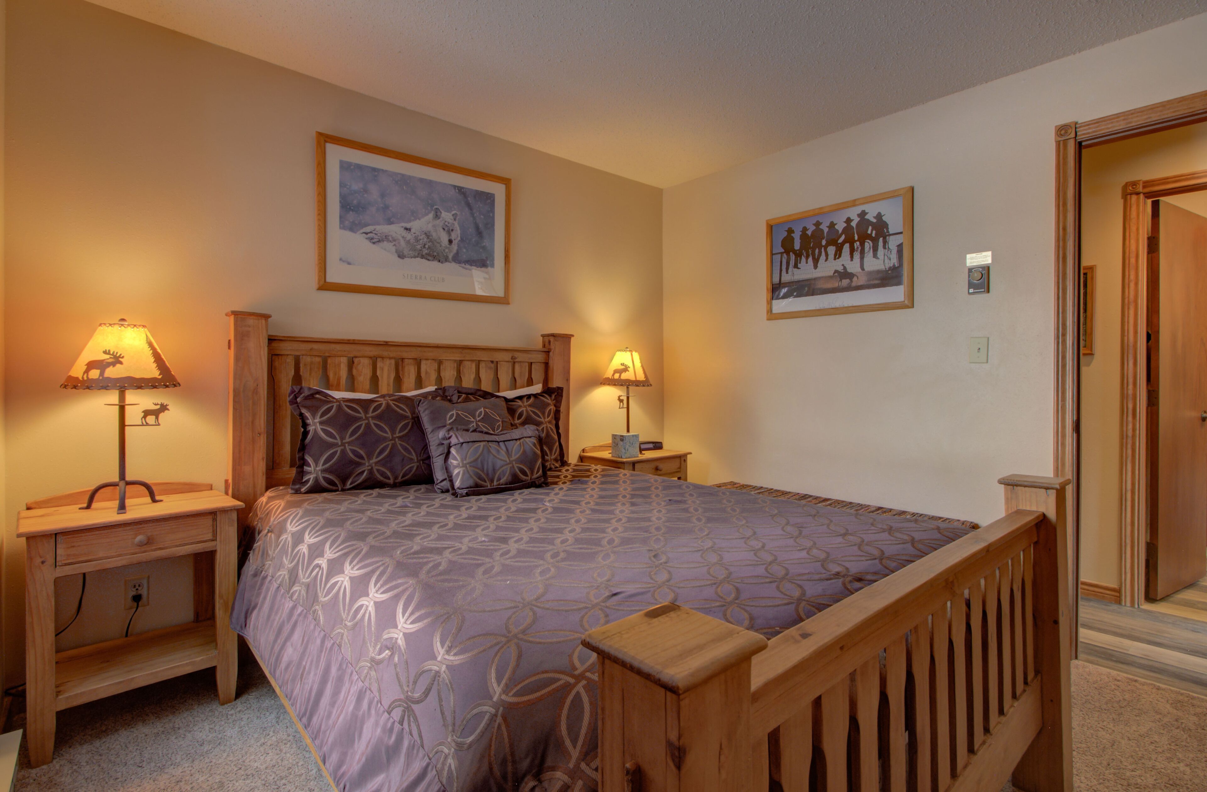 A bedroom with a wooden bed, two bedside tables with lamps, and two framed pictures on the wall.