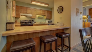 Una cocina con gabinetes de madera, microondas, cafetera y una barra con taburetes.
