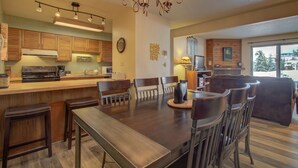Una cocina moderna con armarios de madera, un comedor con una mesa grande y sillas, y una araña.