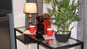 A small table with a coffee maker, two red cups, a lamp, and a potted plant. - Au St Martin 2 (Cholet)