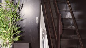 A staircase with a dark wooden handrail leading to a landing. A small white dog is sitting on the landing. - Au St Martin 2 (Cholet)