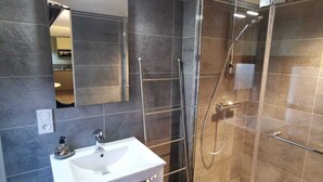 A modern bathroom with a glass-enclosed shower, a white sink, and a mirror above it. - Au St Martin 2 (Cholet)