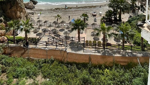 Une plage avec des parasols, des palmiers et une falaise rocheuse.