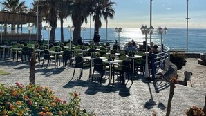 Un espace de restauration en plein air avec des tables et des chaises, des palmiers et une vue sur la mer.
