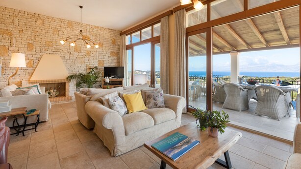 Ein gemütliches Wohnzimmer mit Steinwand, einer Couch, einem Fernseher und einem Balkon mit Korbmöbeln.