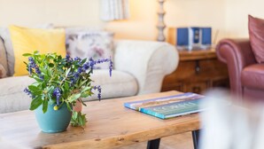 Ein gemütliches Wohnzimmer mit Couch, Kissen, einem Holztisch, einer Zimmerpflanze und einem Bücherregal im Hintergrund.