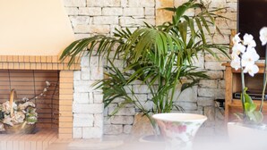 Ein Wohnzimmer mit Kamin aus Stein, einer großen Zimmerpflanze und einer Blumenschale auf einem Tisch.