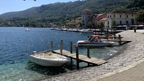 Uma orla marítima com barcos atracados, um caminho de pedras e edifícios ao fundo.