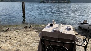 Mesa à beira do lago com toalha, uma cadeira e um barco ao fundo.