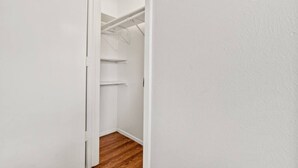 Un pasillo estrecho con piso de madera que conduce a un armario blanco con estantes.
