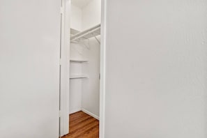 Un couloir étroit, doté d’un plancher en bois, mène à un placard blanc muni d’étagères.
