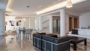 A modern living room with a sofa, coffee table, and dining area. - Blue Oasis Luxury Villa (Malevizi)