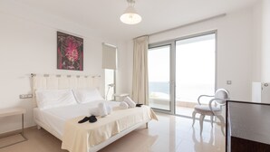 A hotel room with a bed, a desk, a chair, a large window, and a painting on the wall. - Blue Oasis Luxury Villa (Malevizi)