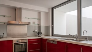 A modern kitchen with red cabinets, a stainless steel oven, a dishwasher, and a large window providing natural light. - Blue Oasis Luxury Villa (Malevizi)