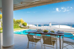A poolside dining area with a view of the sea and cityscape.