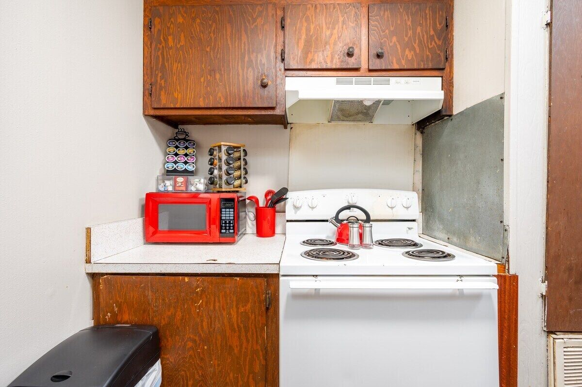 A compact kitchen with wooden cabinets, a white stove, a red microwave, and various kitchen utensils.