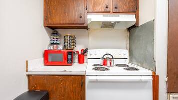 A compact kitchen with wooden cabinets, a white stove, a red microwave, and various kitchen utensils.