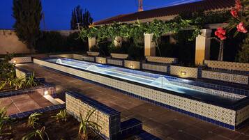 Una piscina con piastrelle blu e bianche, circondata da piante e un pergolato con viti rampicanti.