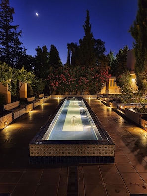A rectangular pool with a tiled border and a central water feature, surrounded by a tiled walkway and decorative plants. - Casa Agostino - Luxury wine resort (Fray Luis Beltrán)