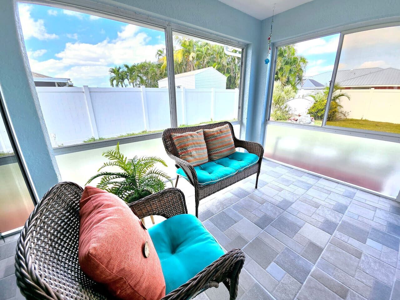 A sunroom with wicker furniture, a view of the backyard, and a tiled floor.