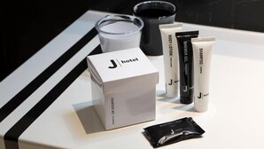 Un baño de hotel con una encimera blanca, una caja de artículos de cortesía, loción corporal, champú y un tubo de gel de ducha.