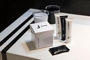 Une salle de bain d’hôtel avec un comptoir blanc, une boîte contenant un kit de produits de courtoisie, une lotion pour le corps, un shampoing et un tube de gel douche.