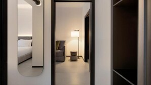 Habitación de hotel con un espejo grande, una cama, un sofá, una lámpara de pie y una pequeña mesa redonda.