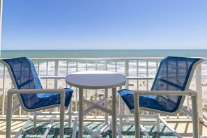 A balcony with two blue mesh chairs and a small round table, overlooking a beach with waves. - Amazing Oceanfront 2 bedroom 2 bath condo Crescent Sands @ Windy Hills (North Myrtle Beach)