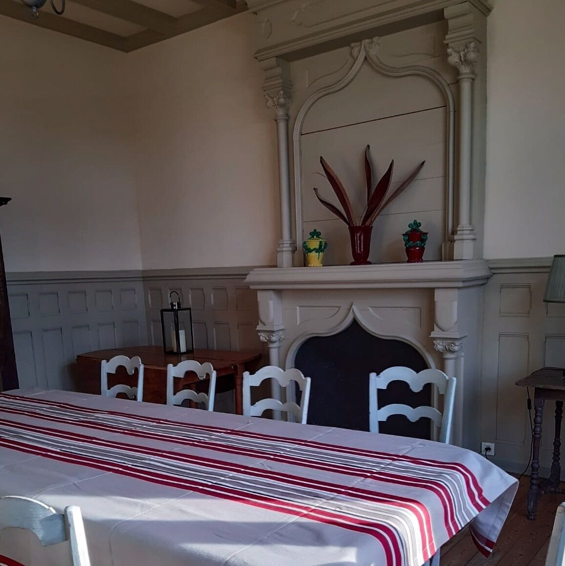 Een eetgedeelte met een tafel gedekt voor vier personen, witte stoelen, een open haard met decoratieve objecten en een witte schoorsteenmantel.
