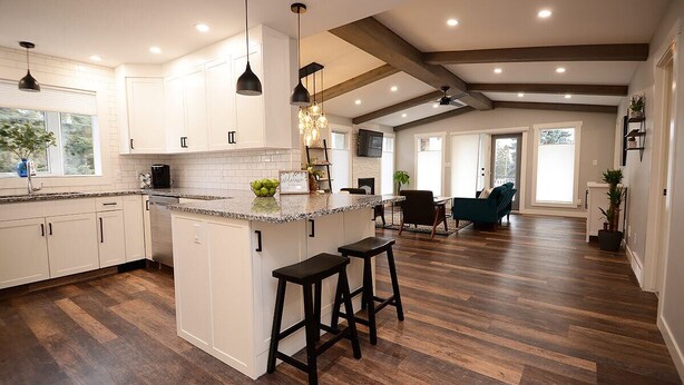 A spacious kitchen with white cabinets, a large island with stools, and a herringbone wood floor.
