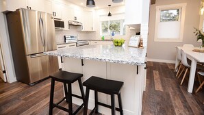 A modern kitchen with stainless steel appliances, a granite countertop, and black bar stools.
