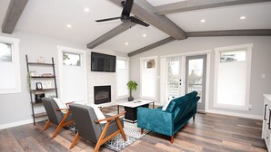 A spacious living room with a fireplace, a ceiling fan, and large windows.