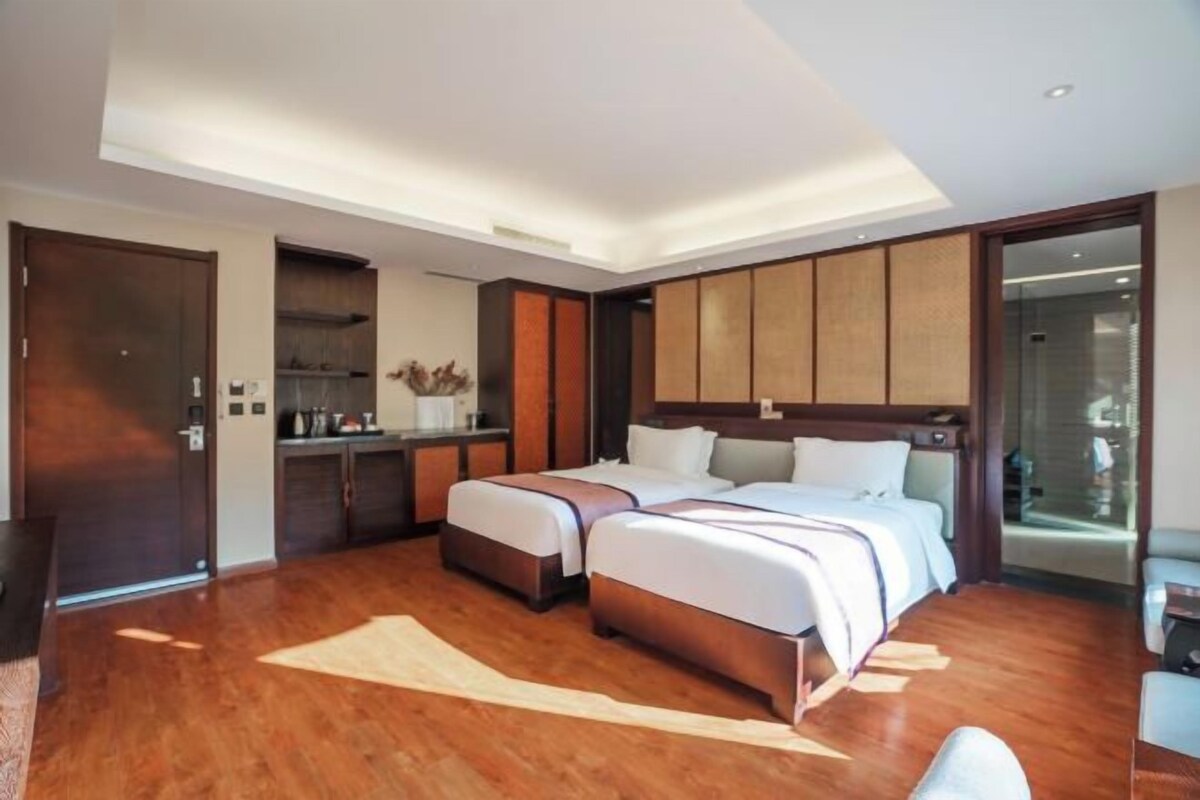 Habitación de hotel con dos camas, una kitchenette pequeña, un amplio acceso corredizo al baño y suelo de madera.