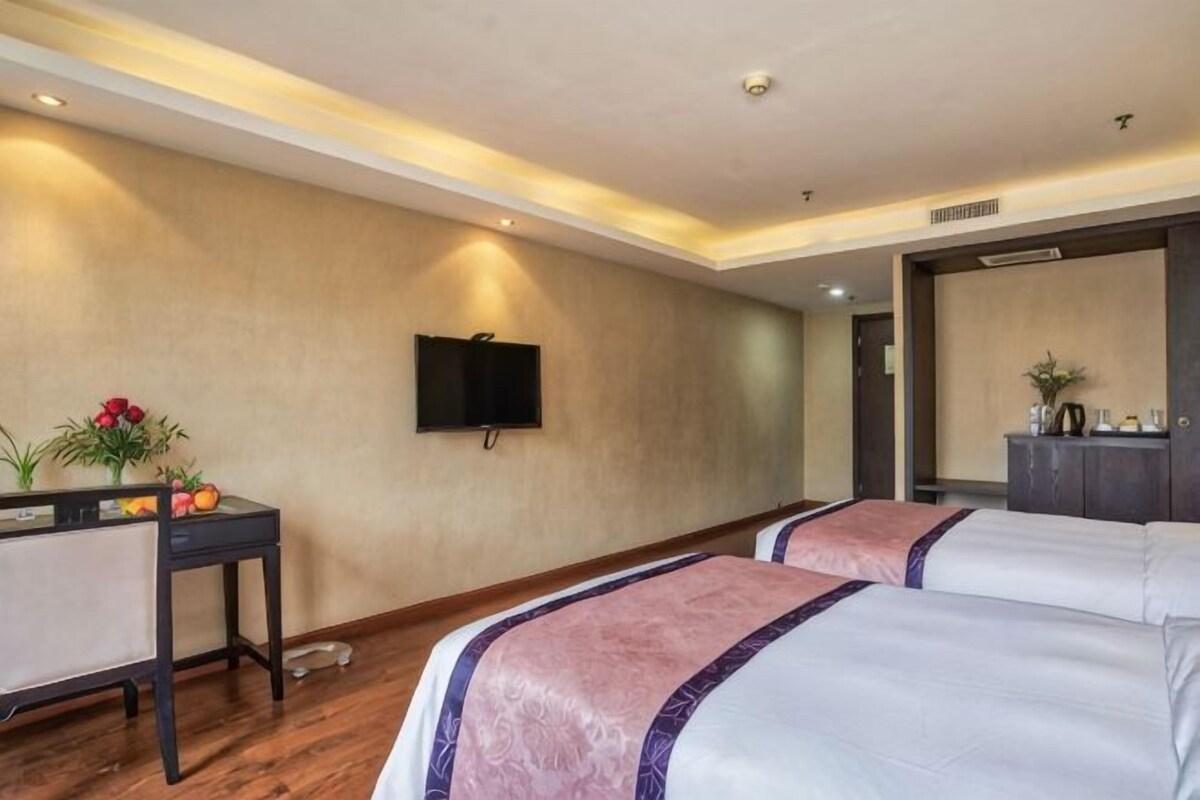 Una camera d'albergo con due letti, una TV, una scrivania con un computer e uno specchio.