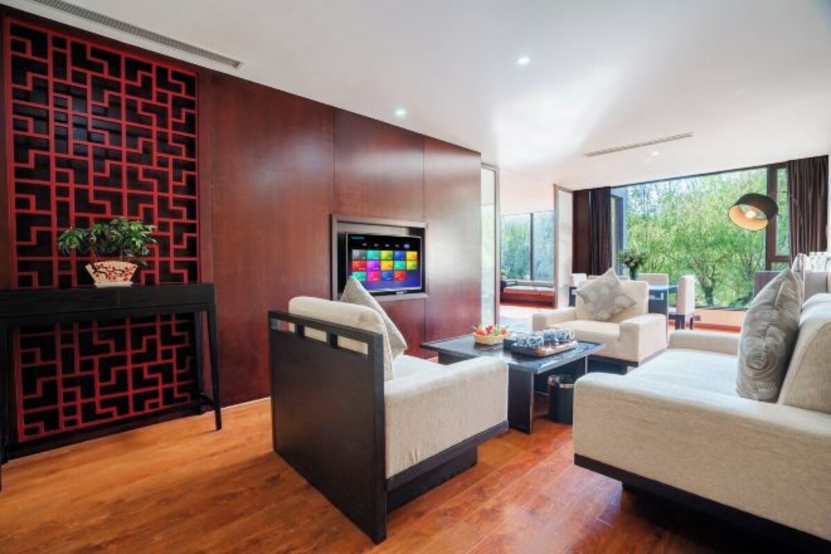 Un soggiorno moderno con un divano, un tavolino e una TV. È presente un pannello decorativo e una finestra con vista sugli alberi.