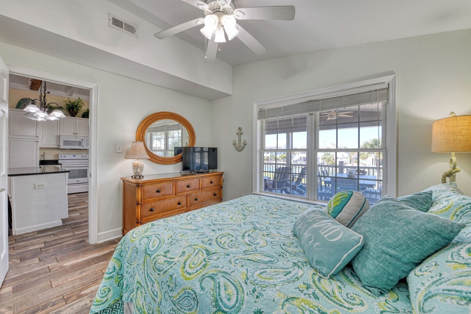 A bedroom with a bed, a dresser, a television, a window with a view, and a ceiling fan.