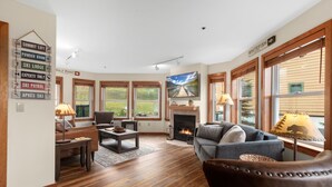A cozy living room with a fireplace, wooden floors, and large windows. - Arguably the best ski in / ski out location in Whitefish!!! AC for hot days (Whitefish)