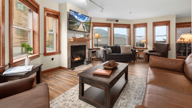 A spacious living room with a fireplace, comfortable seating, and large windows offering a view of the outdoors. - Arguably the best ski in / ski out location in Whitefish!!! AC for hot days (Whitefish)