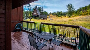 A wooden deck with a metal table and chairs, overlooking a grassy area with a cabin and trees. - Arguably the best ski in / ski out location in Whitefish!!! AC for hot days (Whitefish)