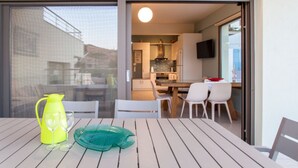 Eine moderne Küche mit Flachbildfernseher, ein Essbereich mit Tisch und Stühlen sowie ein Balkon mit Tisch für zwei Personen.