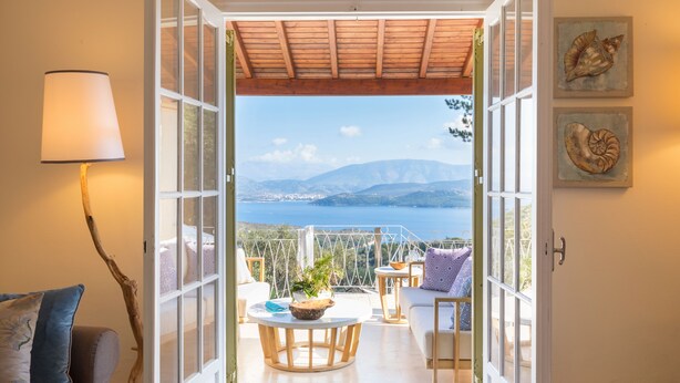 An open balcony with a view of the sea and mountains, furnished with a table, chairs, and a lamp. - Villa Leondari by Rodostamo Collection (Corfu)