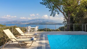 A poolside area with lounge chairs and a table, overlooking a body of water and mountains. - Villa Leondari by Rodostamo Collection (Corfu)