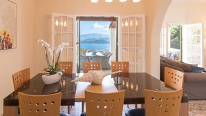 A dining area with a table, chairs, and a view of the sea through an open door. - Villa Leondari by Rodostamo Collection (Corfu)