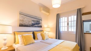 A hotel room with a large bed, two bedside tables with lamps, a painting on the wall, and a window with curtains. - Villa Leondari by Rodostamo Collection (Corfu)