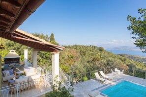 A poolside area with outdoor seating, a barbecue, and a view of the surrounding hills.