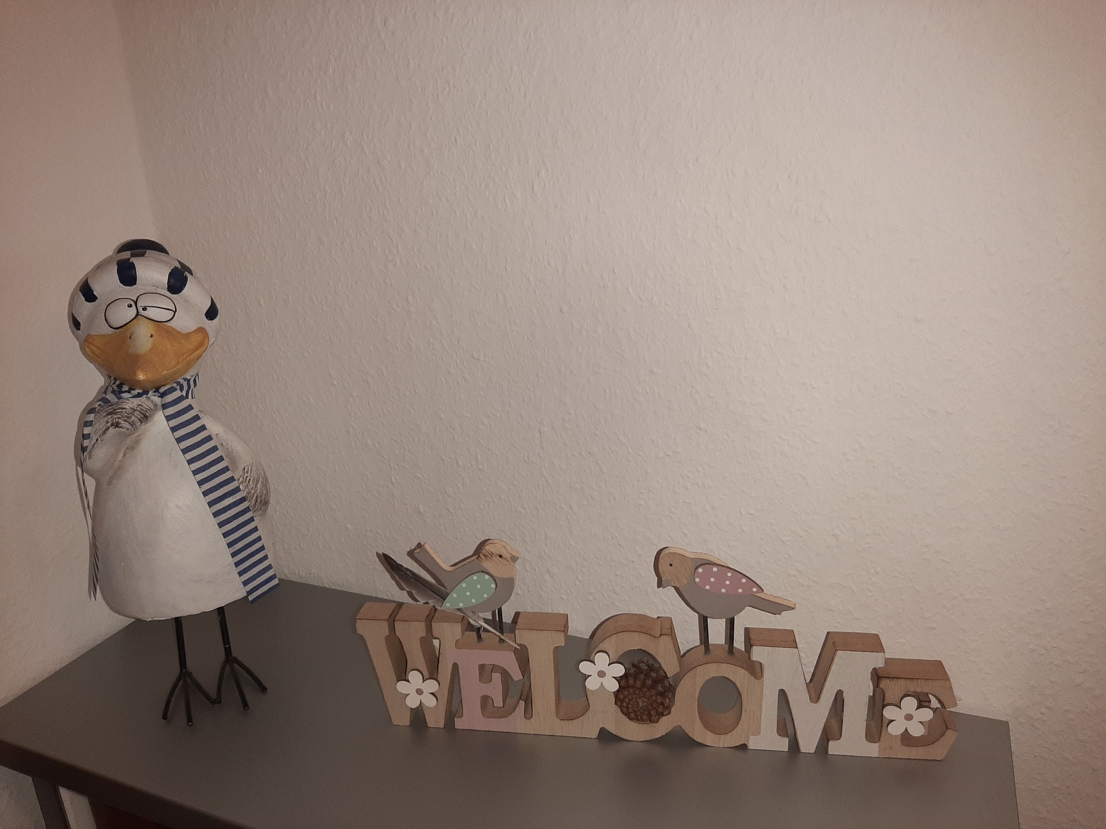 Puinen kyltti, jossa on sana ”TERVETULOA” ja kaksi lintua istumassa sen päällä.