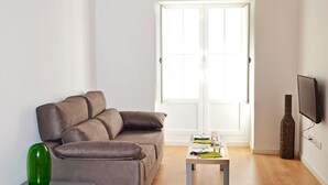 Een woonkamer met een bank, een bijzettafeltje, een groene fles en een televisie.