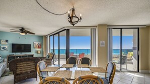 A spacious living room with a glass table, wicker chairs, a ceiling fan, and a TV.
